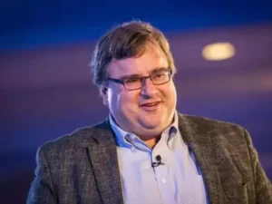 Reid Hoffman in a gray button-up shirt and sleek glasses, arms crossed, against a futuristic digital network background in a professional studio portrait.